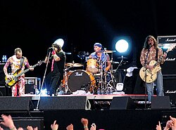 A photograph of four members of the Red Hot Chili Peppers performing on a stage