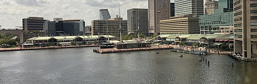 A panoramic viewing of the Harborplace promenade/waterfront in the Inner Harbor, featuring two small malls with green roofs, the Pratt Street Pavilion (left, alongside a blue-green building known as The Gallery at Harborplace) and the Light Street Pavilion (middle right).
