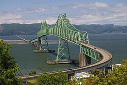 A green-colored truss bridge with two towers crossing a wide river as seen from a distance.