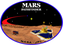 An image inside an oval, depicting two spacecraft, one a lander, and one a rover, on the surface of Mars. The words "Mars Pathfinder" are written on the top and the words "NASA · JPL" are written on the bottom.