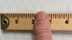 Man's thumb on a wooden ruler that is marked in inches