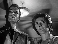Shatner and Jeanne Cooper are looking beyond the camera in a stern manner.