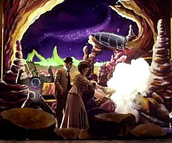 The set from the "Tonight, Tonight" music video features the performers dressed in Victorian clothing on a colorful set mimicking the moon. A moon monster is portrayed by a man on the left of the photo; he has on a pale green form-fitting jumpsuit with large blue and purple dots on it and wears matching make-up. On his head is a large prosthesis mimicking tall pale green hair. A man stands to the right wearing a suit and bowler and in front of him is a woman wearing a flowing gown. The woman has just struck another moon monster with an umbrella, and the moon monster has disappeared in a puff of smoke.