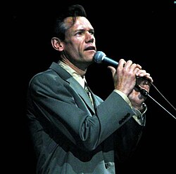 Randy Travis, wearing a gray suit while singing into a microphone