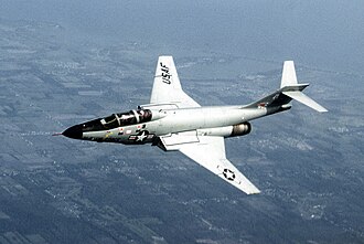Photo of F-101 aircraft flying. On the aircraft's side is a symbol with a star, to the left of which says, U.S. Air Force. Its horizontal stabilizers are located atop its fin.
