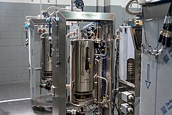 A stainless steel single-use bioreactor system, featuring integrated sensors and tubing, located in a Factory Acceptance Testing (FAT) room.