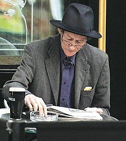 Alex Higgins seated at a table, reading a newspaper