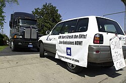 An SUV (RAV4 EV) with a poster that reads "GM Don't Crush the EV1s! Zero Emissions NOW!