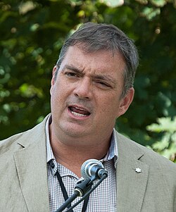 Tim Cook at the Eden Mills Writers' Festival in 2017, medium shot of a caucasion male in their 40s, with greying hair, and Shure Brothers SM58 microphone in front of him.