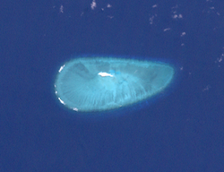 Satellite image of a small sand island at the centre of an oval-shaped reef