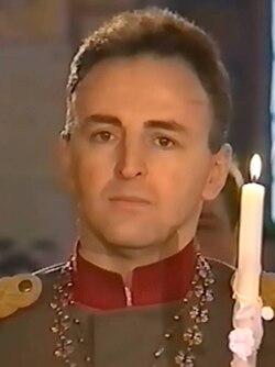 Headshot of Arkan in a green uniform, holding a candle up to his face