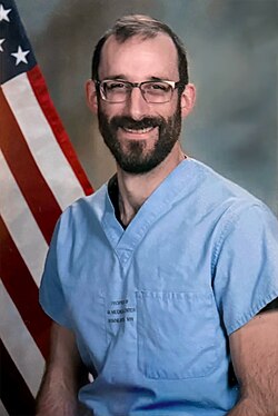 Headshot of a bearded Pretti wearing glasses and smiling against a white background