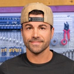 Headshot of Mark Rober in front of his workbench. He is a white man with short dark and a stubble beard, wearing a light backwards cap and a black T-shirt.