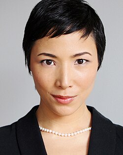 close-up of Julee Cerda wearing a black, open-necked top and pearl necklace, looking directly at camera with slight smile