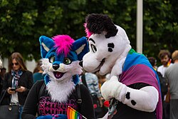 Two people wearing fursuits holding and wearing pride flags