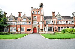A mock Tudor, red brick building with crenellations in white stone and a central tower.