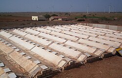 The condenser at Satapar in India consists of eleven ridges. The ridges are trapezoidal in section (top 50 cm, base 200 cm, two sides sloping 30-degree from horizontal, height 100 cm) and each is 20 m long. The ridges are built over gently sloping ground. All the ridges drain into a common pipe at the lower and leading to storage below ground. Water for use is withdrawn by a hand pump. The system was commissioned in early April 2007. Total cost of the installation was Rs 117,000.