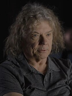 close-up of Jerry Harrison wearing a dark sleeveless top, looking left of camera with a set facial expression