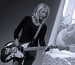 A woman plays a guitar in front of a projection screen.