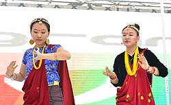 alt=Kauda/Chudka dance performance at Everest sending letters to each other.   Syahi-Syahi is oftenly used in Kauda chudka music but dont have its proper meaning while singing and dancing in this event. Talking about the authenticity of the Kaura performance, “The female dancers should be in odd number, starting from minimum three to maximum 13. Only unmarried women were allowed or considered suitable to participate in the performance, while both married & unmarried men could perform. In Kaura, one verse is sung multiple times to create rhythm for the dancers. It was often mandatory for men to sing to the rhythm of the instrument Khaijandi while women to dance, wearing Jharra in their legs. Although associated with its distinctive costume, musical instruments and prosody, some have expressed concern that Kaura is losing its authenticity due to perversions introduced by commercialization and external influence, while others have been more optimistic deeming the changes a natural part of the cultural evolution and increasing popularity.[1] New York 2019