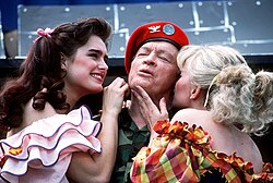 Comedian Bob Hope in the center. Singer Barbara Mandrell is kissing his left cheek, while actress Brooke Shields is stroking his right cheek.