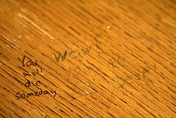 Written on a wooden desk, "You will die someday" a response is next to it.