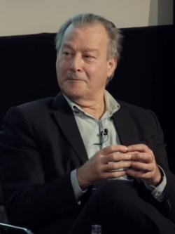 Half-length photo of Jonathon Green sitting on a chair while holding his fingers together