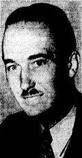 Black-and-white photographic portrait of a smiling man with slicked-back hair and a divided toothbrush mustache.
