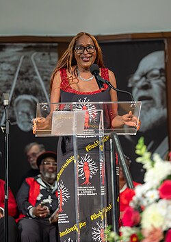 Janetta Johnson speaking at Glide Memorial Church wearing a dress with the TGIJP logo