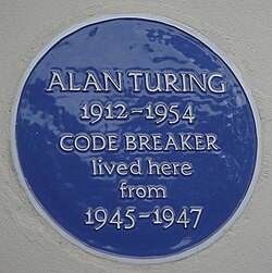 A Blue plaque on a white wall with the words "Alan Turing 1912–1954 CODE BREAKER lived here from 1945 – 1947