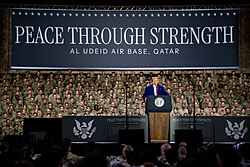 Donald Trump in front of a peace through strength banner