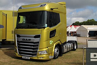 A yellow low-deck next generation DAF XG in a DAF stall at a truck show. It is a 2-axle chassis with dual tyres on axle two and a high capacity fuel tank
