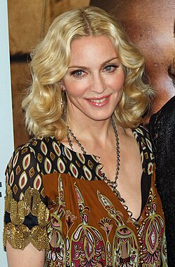 Madonna wearing a loose dress, looking to the right and smiling.