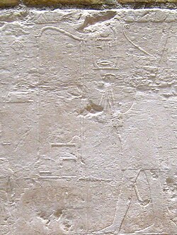 Relief showing a king seated on a throne, wearing a tight fitting dress and holding a flail. He is surrounded by hieroglyphs.