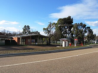 Shop, no longer operating; a wall with post office boxes is in the foreground with the post box and public phone