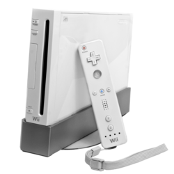 A video game console with mostly white with a glossy finish, featuring a small, vertical form factor. At the front, there is a vertical slot where the discs are inserted. Leaning on the right side is a white, rectangular handheld controller.