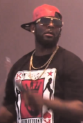 R. Kelly, with a half-backwards cap and sporting chains, swings his microphone at a concert.