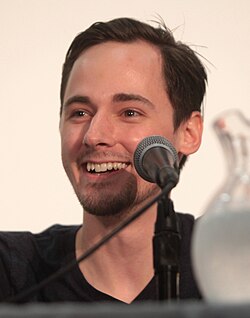 Thomas glancing away from a camera and smiling