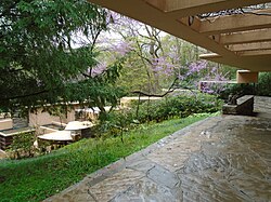 A view toward Fallingwater's main house from an outdoor path just outside its guest wing. The path is covered by a canopy. The main house can be seen down the hill.