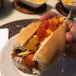 In Brazil, a cachorro quente is served on a bread roll with a tomato-based broth, corn, and potato sticks.