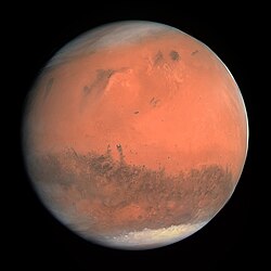 An image of the planet Mars. It is round and has a largely red color. The top and bottom of the planet are coated white.