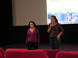 Two women stand in front of a screen in a movie theater