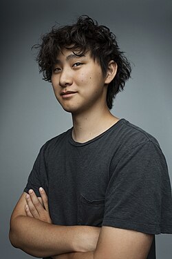 Studio portrait of Wang wearing a dark gray T-shirt, with a gray background