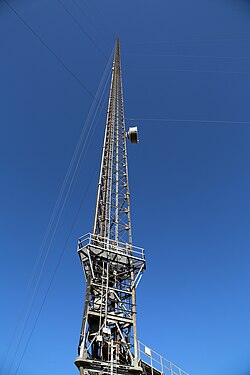 A tall, gray, metal tower with guy wires against a blue sky