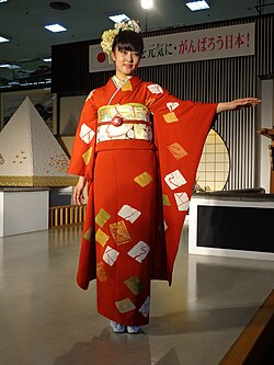 A young unmarried Japanese woman wearing a deep orange furisode with her arms outstretched.