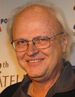A profile image of Dennis Muren. A middle-aged, balding Caucasian male with short-white hair on the sides of his head. He is wearing dark glasses and looking towards the camera with a smile.