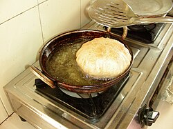 A puri floats in oil, which fills a rounded pot on a stove.