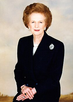 Half-length portrait of Thatcher. She is wearing a black suit and pearls, with a brooch on her left lapel. Her hands are clasped in front of her, adorned with rings. The background is pale and softly lit.