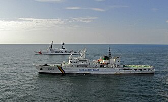 A Korea Coast Guard vessel training with a US Coast Guard vessel, in the distance