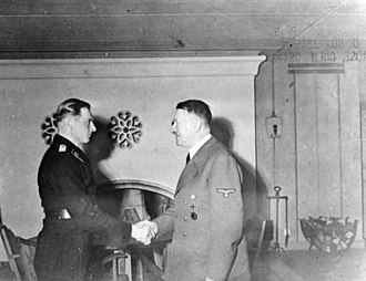 Wittmann, standing on the left, is shown receiving his Knight's Cross of the Iron Cross from Adolf Hitler standing on the right.
